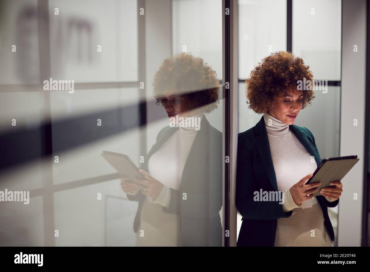 Prise de vue en soirée d'une femme d'affaires enceinte debout dans le couloir du moderne Bureau utilisant une tablette numérique Banque D'Images