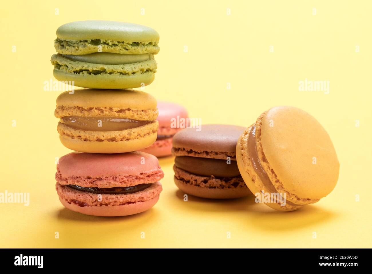 Pâte de macarons français pastel aux saveurs de framboise, citron, chocolat et pistaches sur fond jaune clair Banque D'Images