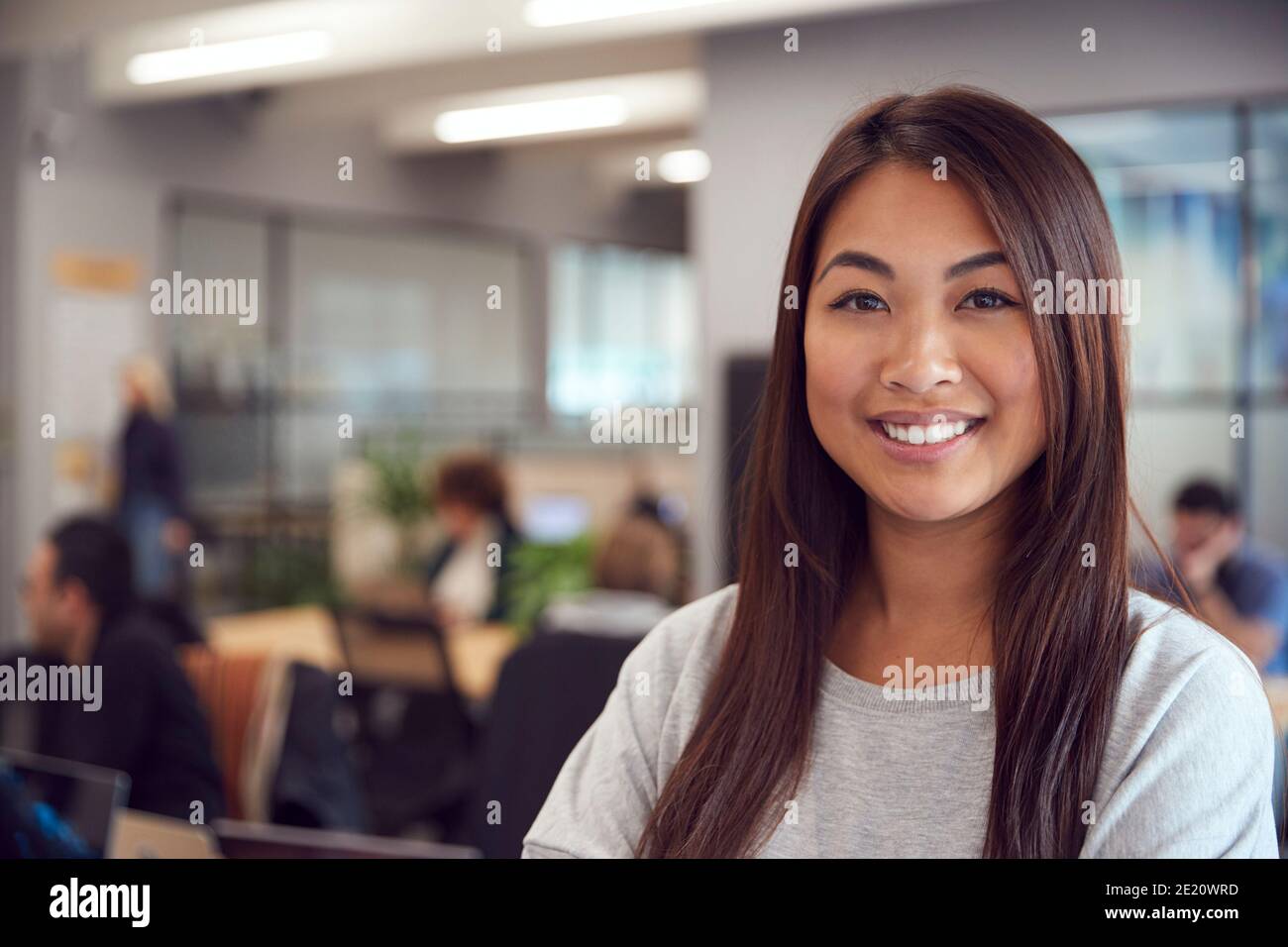 Tête et épaules Portrait de Smiling Young Asian Businesswoman Working Dans un bureau moderne très animé Banque D'Images