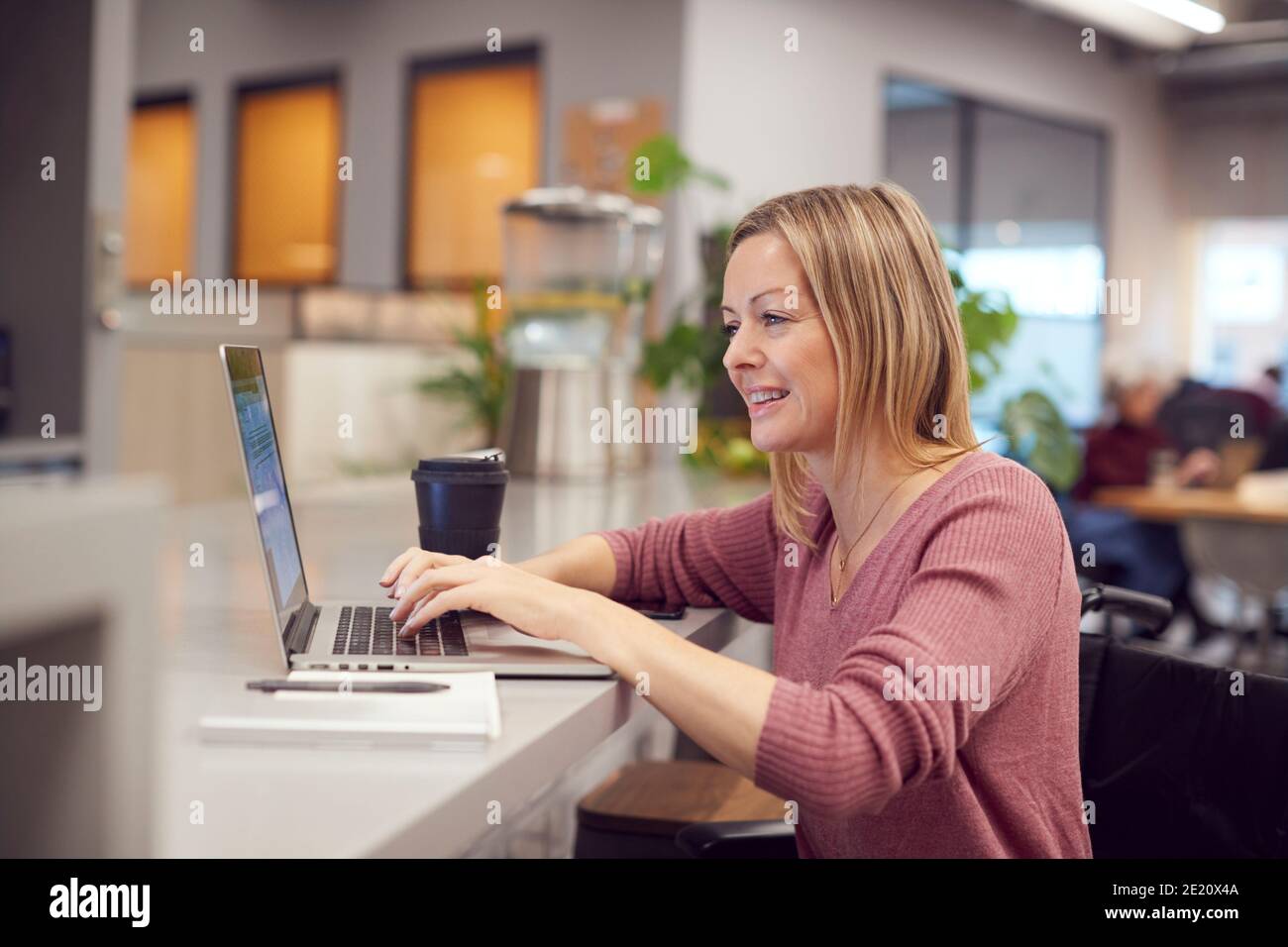 Femme d'affaires en fauteuil roulant travaillant sur un ordinateur portable dans la cuisine de Bureau moderne très fréquenté Banque D'Images