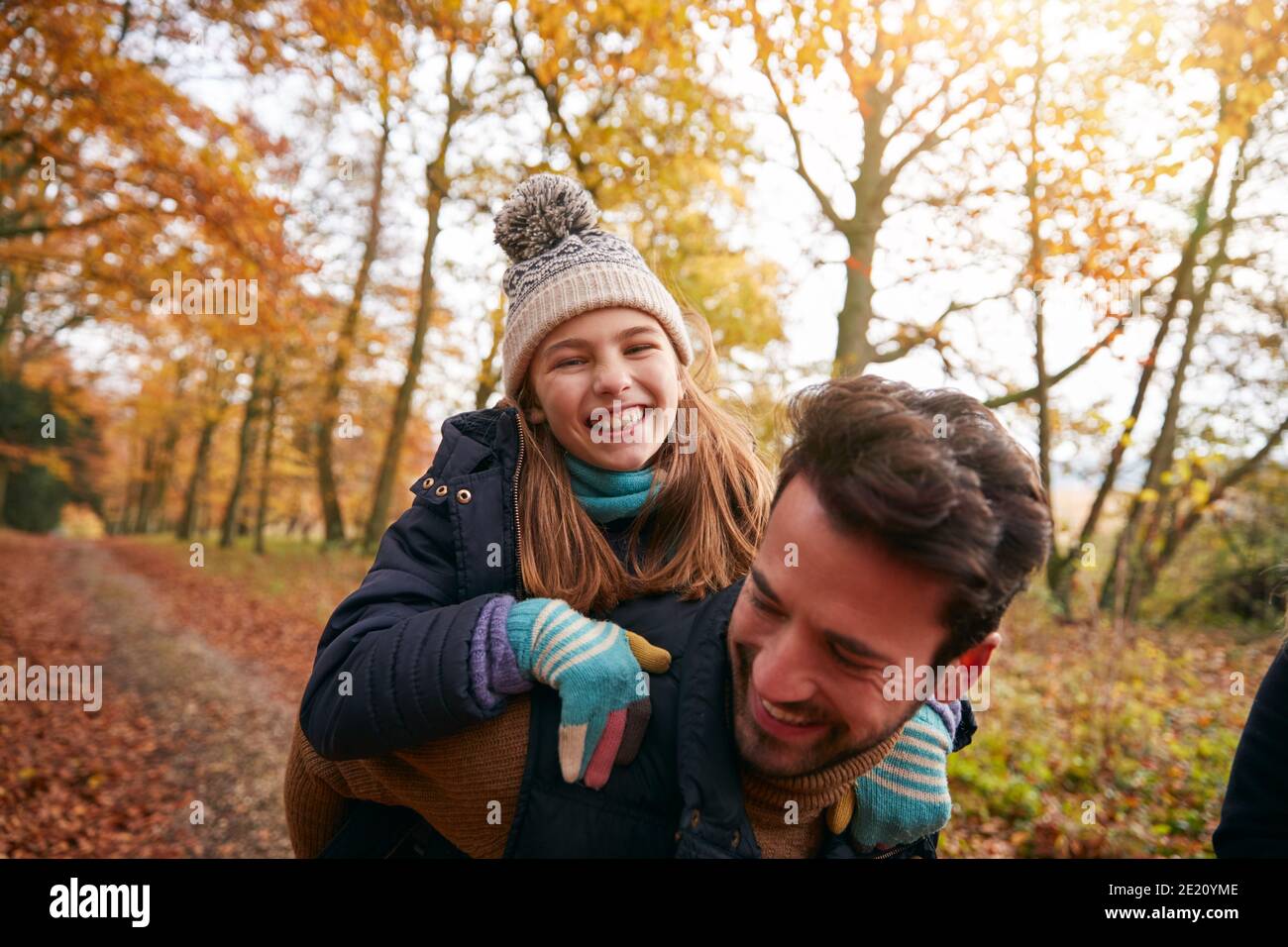 Père donnant rire fille Piggyback Ride sur la famille à travers Forêt d'automne Banque D'Images