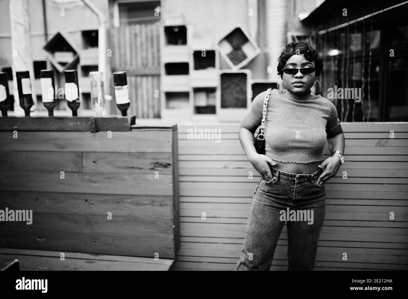 Jeune femme afro-américaine urbaine en haut rose et gris jeans et lunettes de soleil avec sac à main. Afro mode chic femmes. Banque D'Images