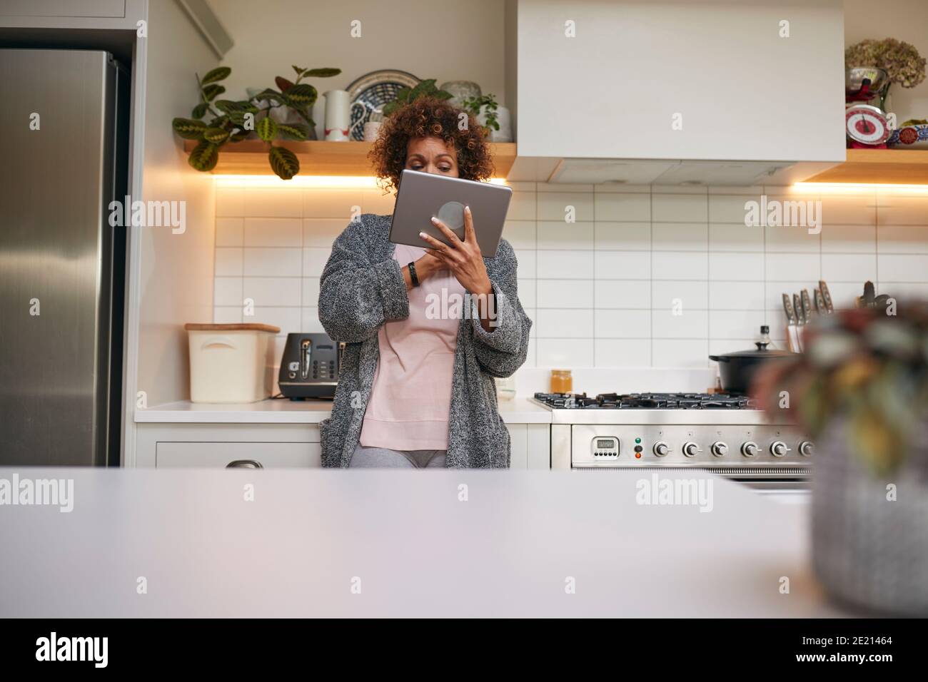 Femme afro-américaine mature en pyjama à la maison dans la cuisine En regardant la tablette numérique Banque D'Images