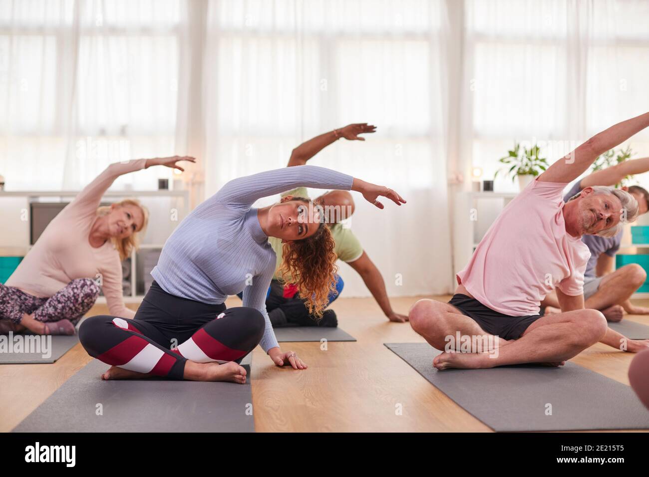Groupe avec un professeur assis sur des tapis d'exercice s'étirant en yoga Classe à l'intérieur du centre communautaire Banque D'Images