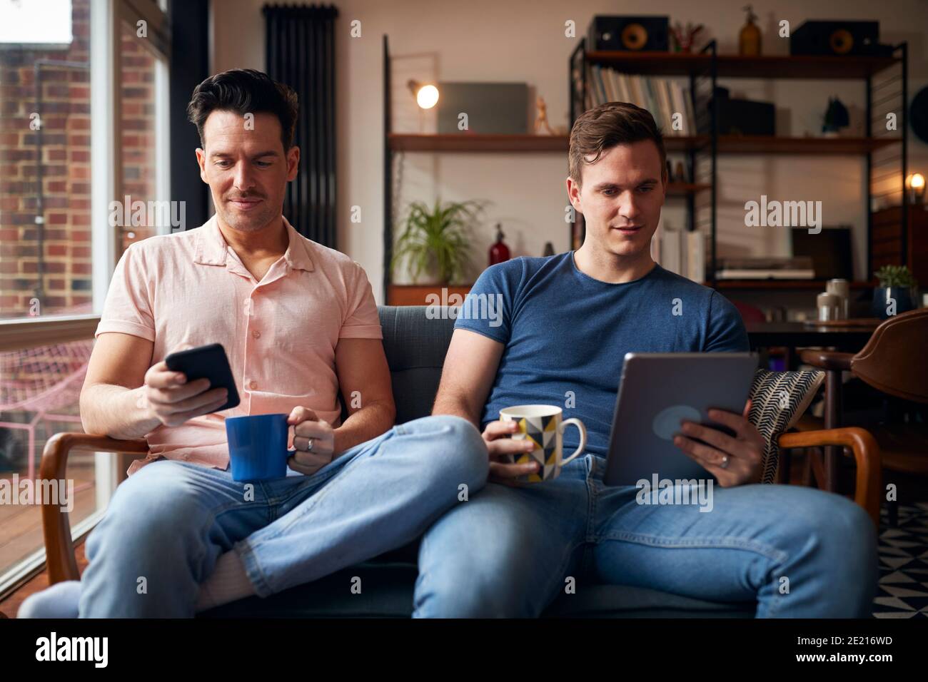 Même sexe Homme couple assis sur un canapé en utilisant la tablette numérique Et le téléphone mobile pour se détendre à la maison Banque D'Images