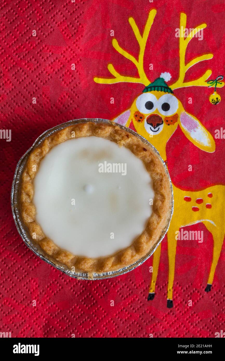 Tarte aux pommes de terre hachée glacée de Sainsburys sur une serviette de Noël festive - pâtisseries fourrées de viande hachée, recouvertes de glaçage blanc doux Banque D'Images