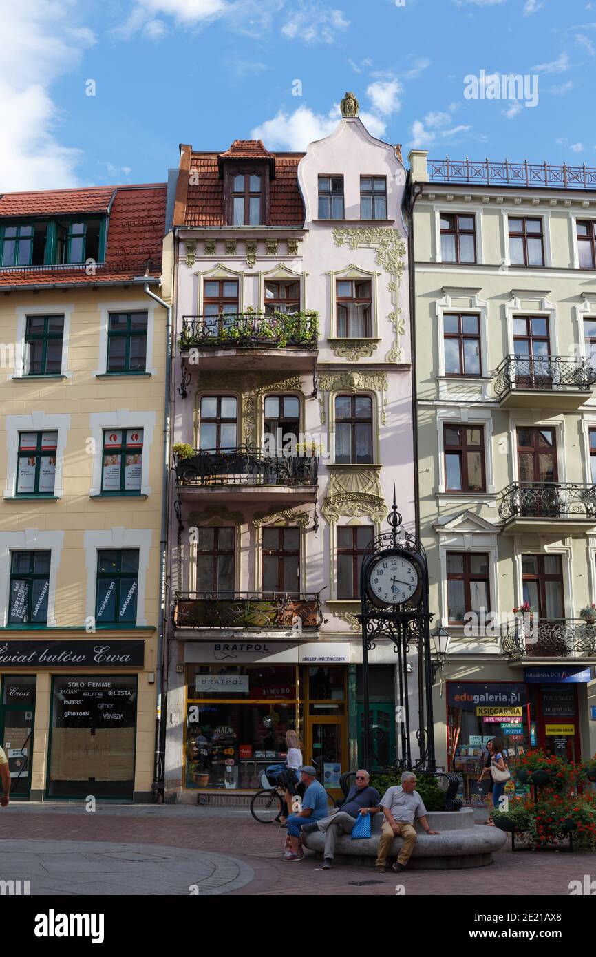 La rue Torun, les bâtiments de la maison, les magasins et un groupe d'hommes se sont assis à l'extérieur en dessous d'une horloge, Pologne Banque D'Images