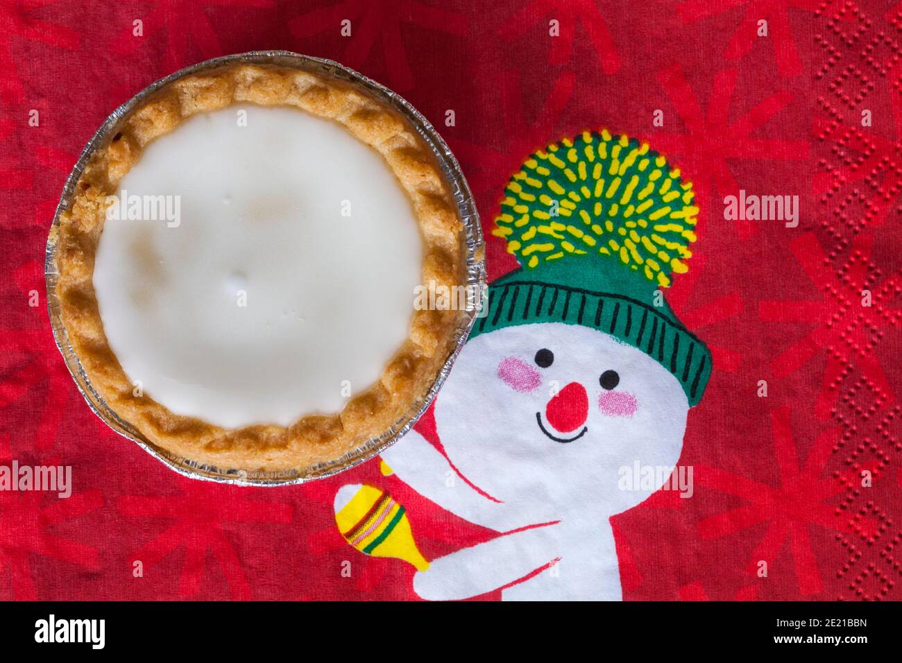 Tarte aux pommes de terre hachée glacée de Sainsburys sur une serviette de Noël festive - pâtisseries fourrées de viande hachée, recouvertes de glaçage blanc doux Banque D'Images