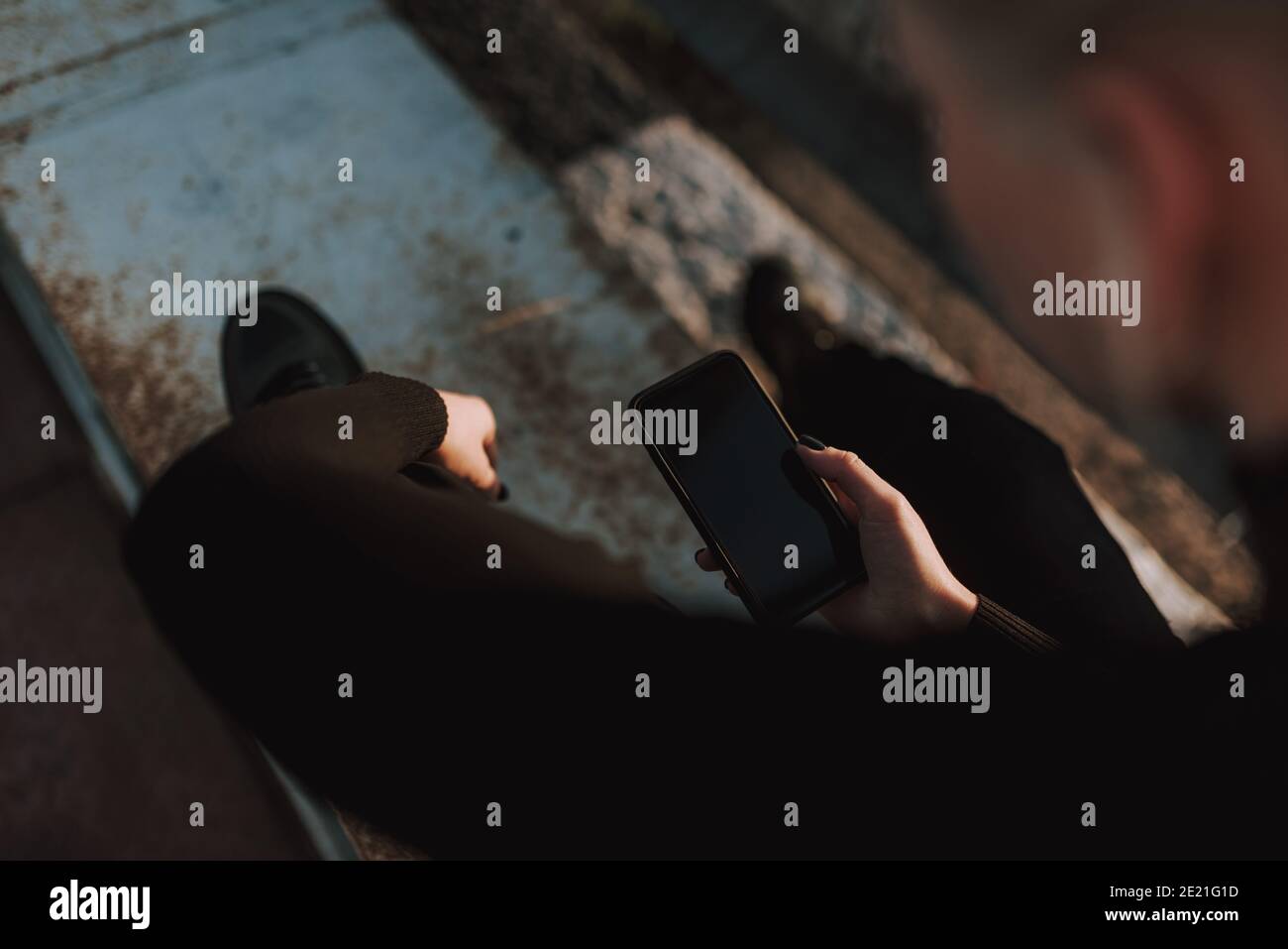Vue de dessus des mains de dame en utilisant un smartphone tout en étant assis en métal construction à l'extérieur Banque D'Images