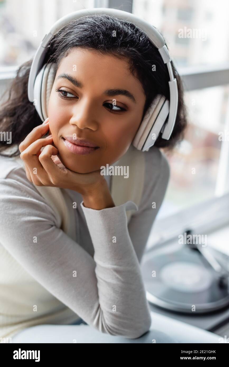 femme afro-américaine pensive écoutant de la musique dans des écouteurs sans fil à accueil Banque D'Images