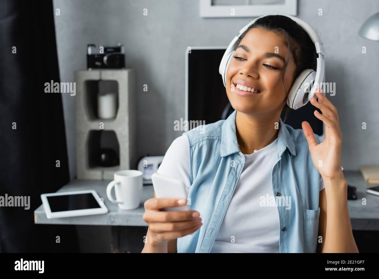 un freelance afro-américain souriant écoute de la musique dans un casque sans fil tenir votre smartphone à la maison Banque D'Images