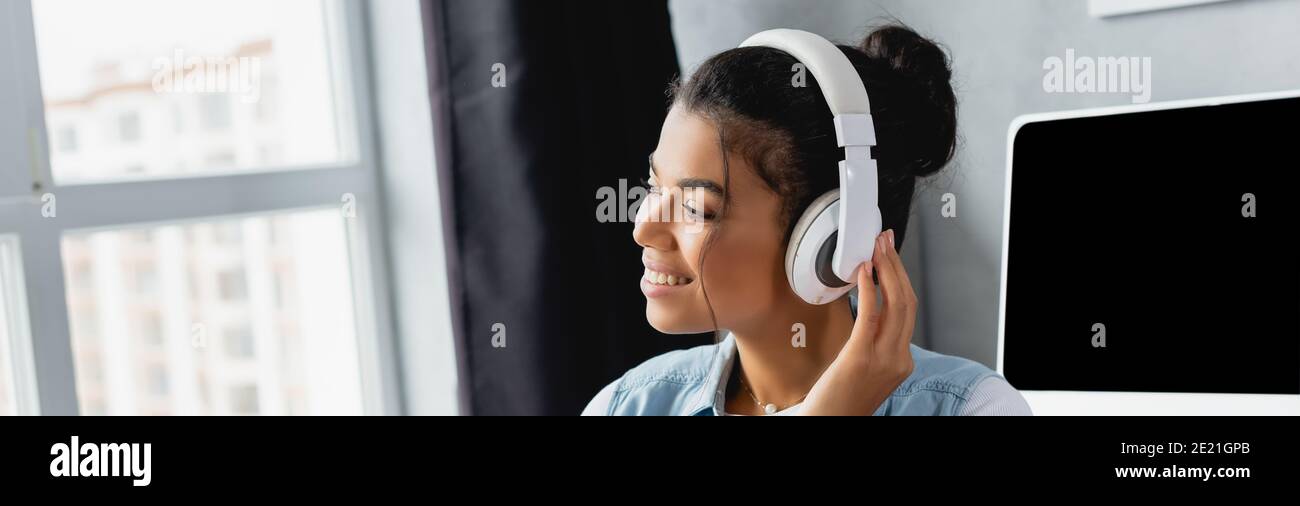 joyeuse femme indépendante africaine écoutant de la musique dans des écouteurs sans fil à la maison, bannière Banque D'Images