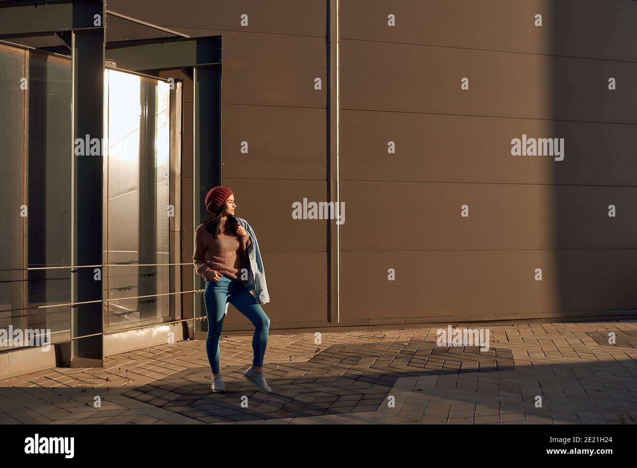 Jeune femme brune confiante et belle en tenue élégante en denim pose à l'extérieur près d'un bâtiment moderne Banque D'Images