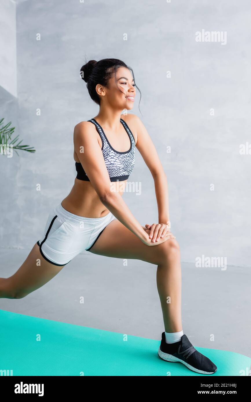 joyeuse femme africaine américaine dans les vêtements de sport faisant  avant fente exercice sur le tapis de fitness à la maison Photo Stock - Alamy