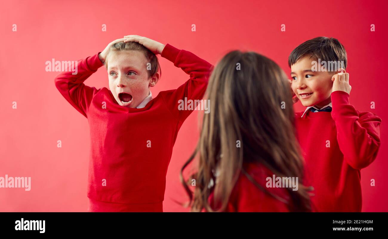 Groupe d'élèves enthousiastes de l'école élémentaire portant un uniforme ayant du plaisir Sur fond Red Studio Banque D'Images