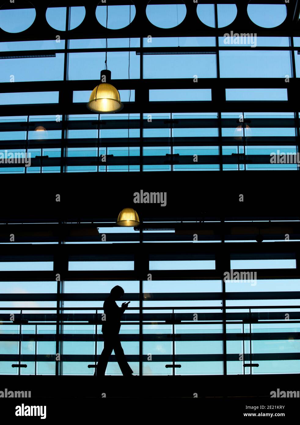 Une personne marche silhoueté contre les fenêtres de l'architecture moderne. Banque D'Images