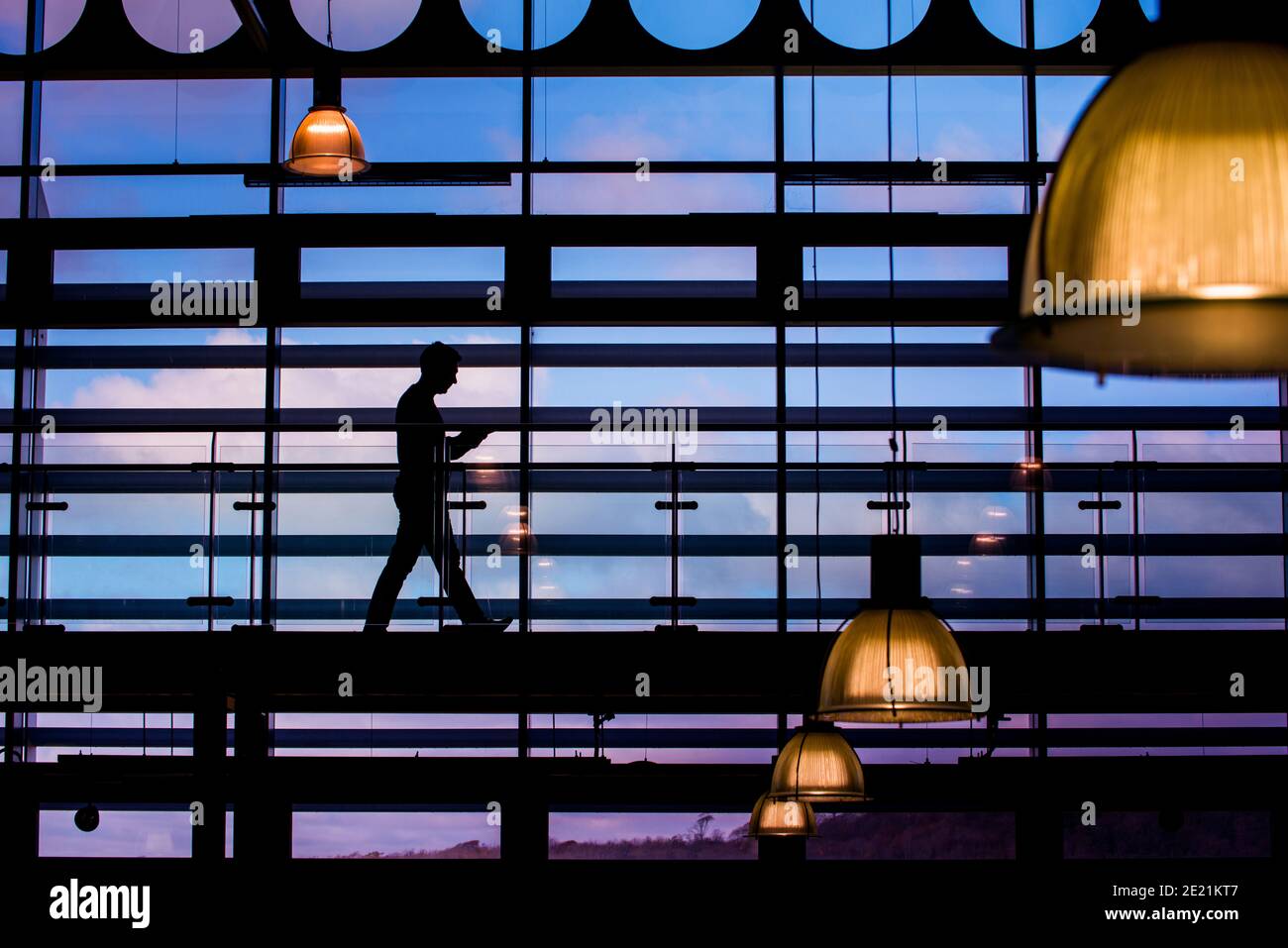 Une personne marche silhoueté contre les fenêtres de l'architecture moderne. Banque D'Images