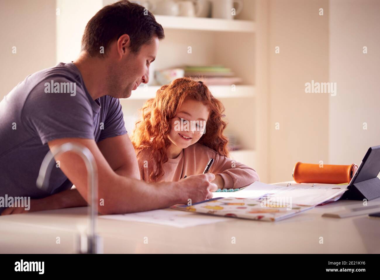 Père aidant la fille avec le travail à domicile assis au comptoir de cuisine en utilisant Tablette numérique Banque D'Images