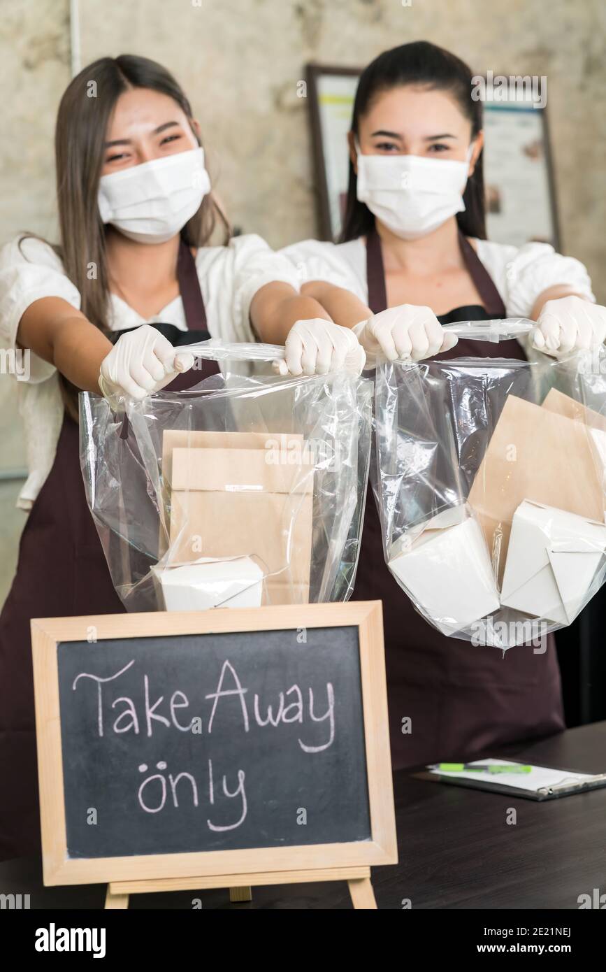 Une serveuse en gros plan porte un masque facial protecteur sourire et tient le sac à provisions pour les plats à emporter ou à emporter. Ce service essentiel est très populaire tandis que ci Banque D'Images