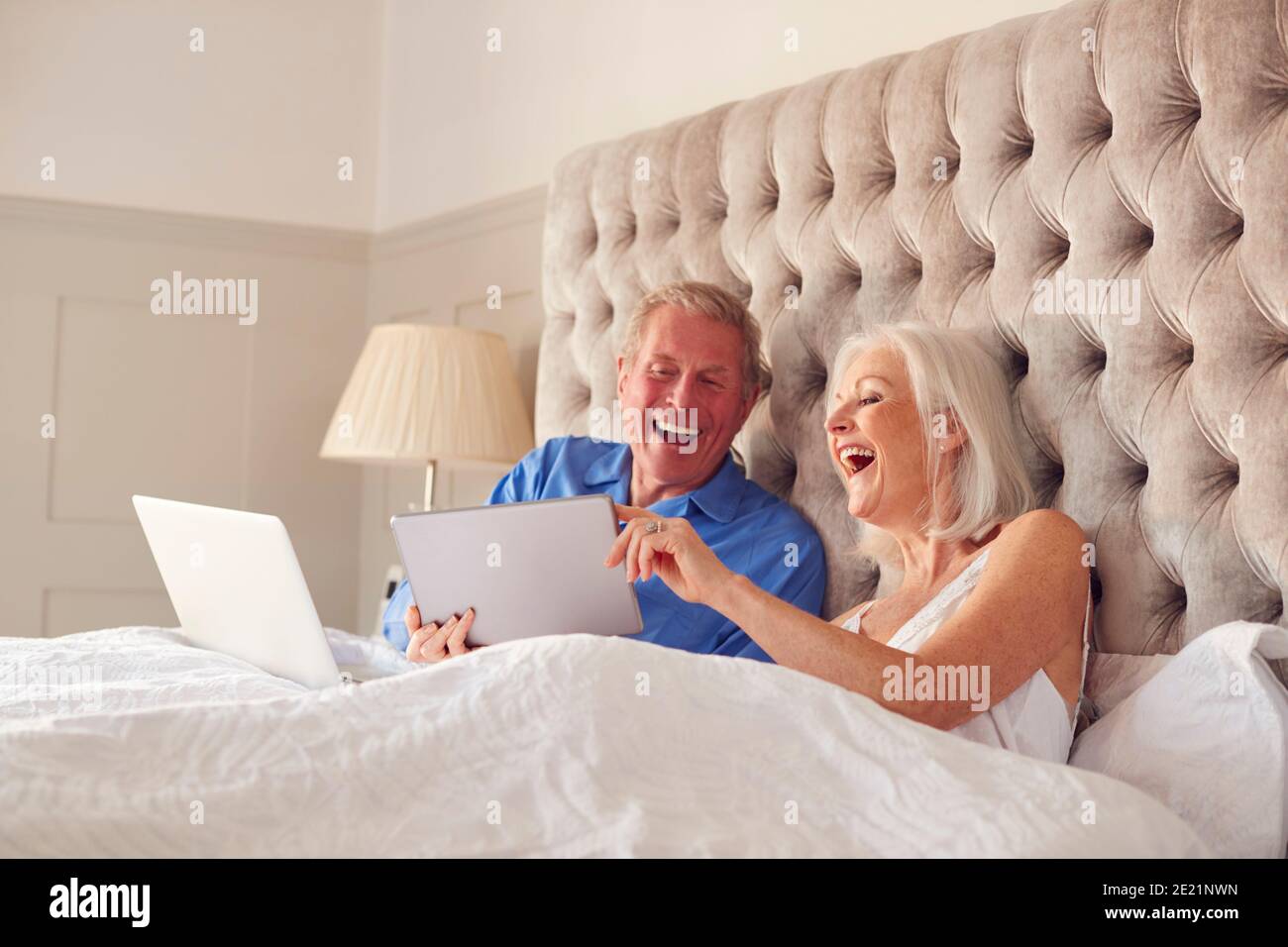 Couple senior à la maison dans le lit auto-isolation à l'aide du numérique Tablette et ordinateur portable pendant le verrouillage Covid 19 Banque D'Images