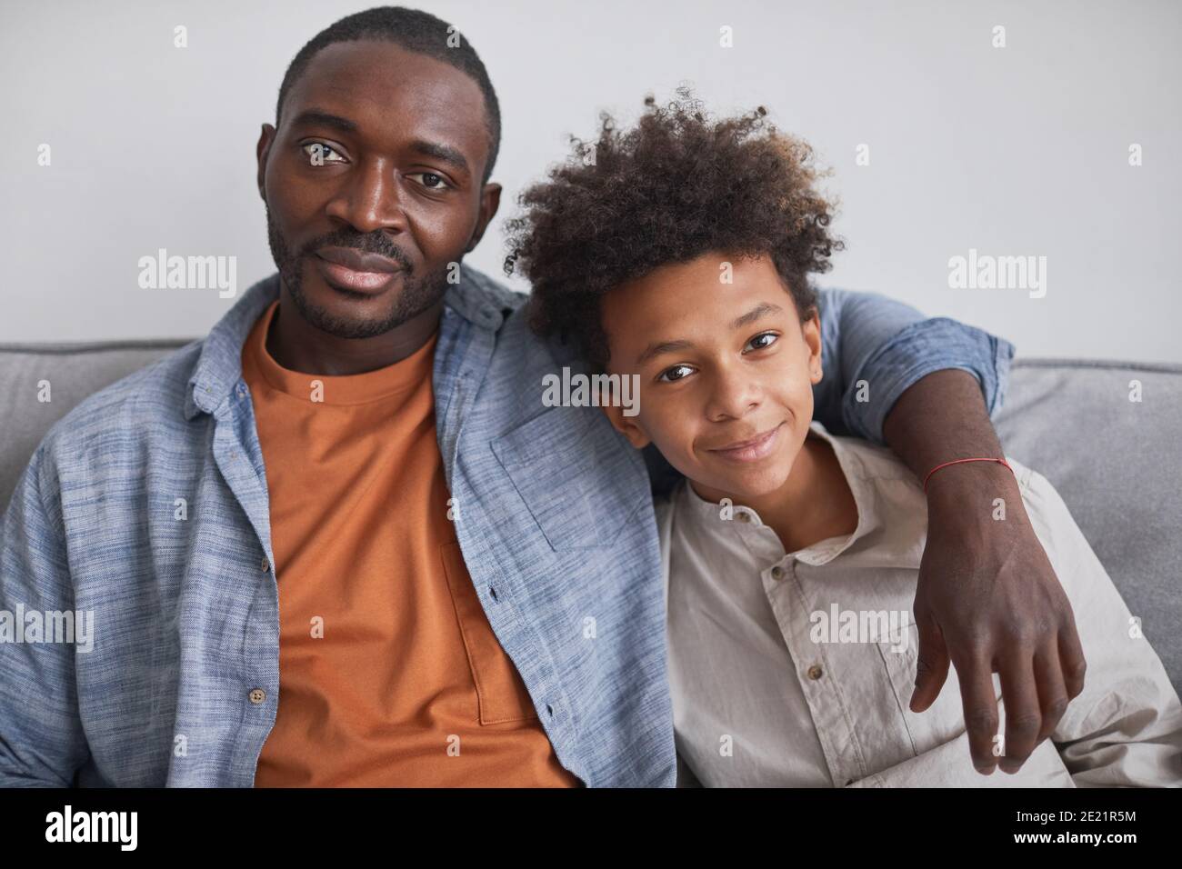 Portrait de l'homme afro-américain heureux à la taille assis sur un canapé avec son fils adolescent regardant la caméra Banque D'Images