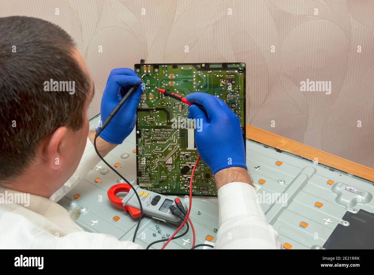 L'ingénieur électricien utilise un multimètre pour mesurer la résistance sur la carte de circuit imprimé verte du centre d'entretien. Réparation du moniteur LCD. Mise au point sélective. Banque D'Images