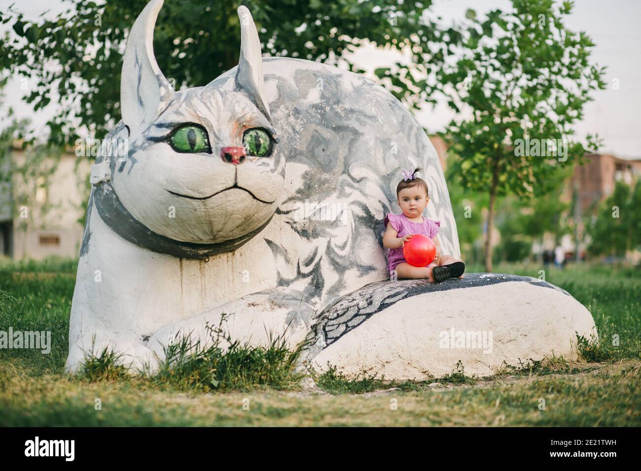 Plan Long D Un Bebe Mignon Assis Dans Un Parc Public Sur La Statue De Chat De Pierre Et Tenant Le Ballon Rouge Photo Stock Alamy