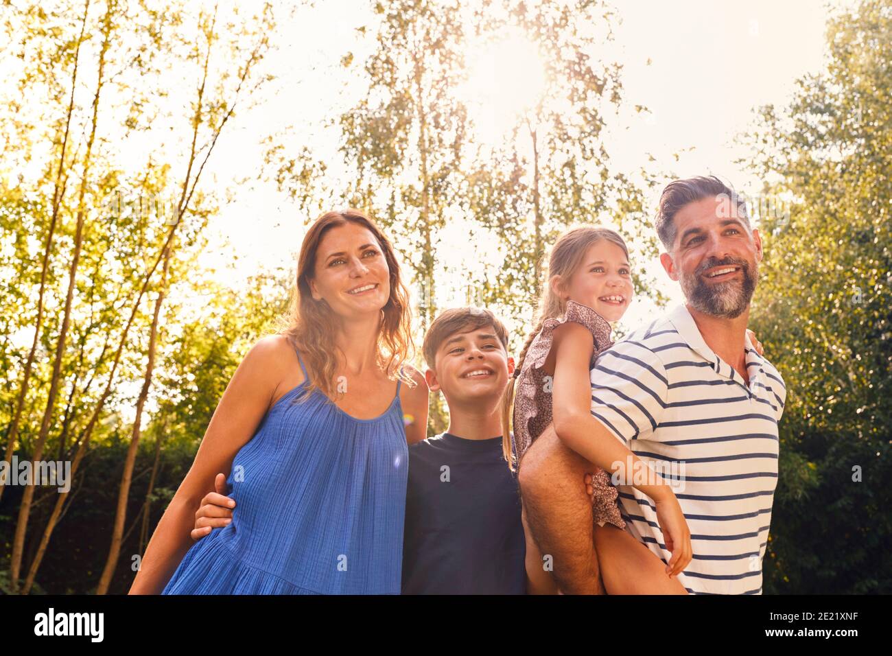 Portrait de famille souriante dans le jardin d'été avec le Père donner Fille Piggyback Ride sur le dos Banque D'Images