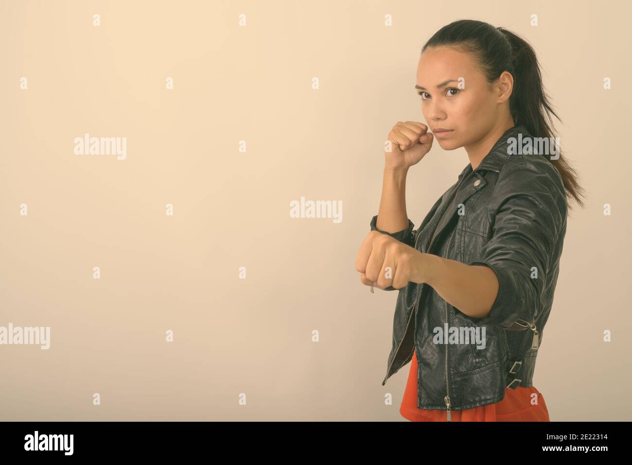 Photo studio d'une jeune femme asiatique qui regarde sur le côté avec les deux poings élevés prêts à se battre contre fond blanc Banque D'Images