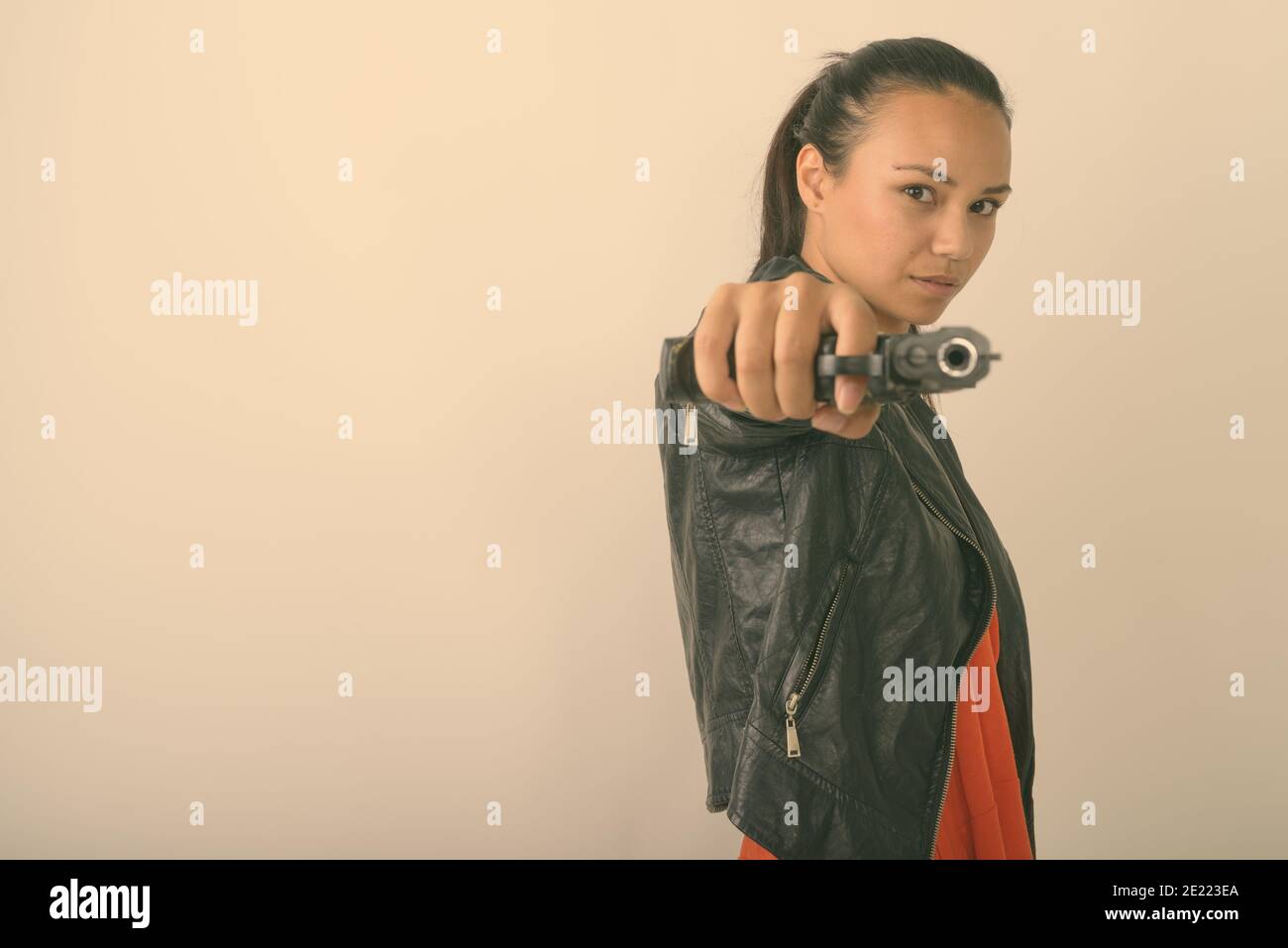 Photo en studio d'une jeune femme asiatique visant une arme de poing à la caméra sur fond blanc Banque D'Images