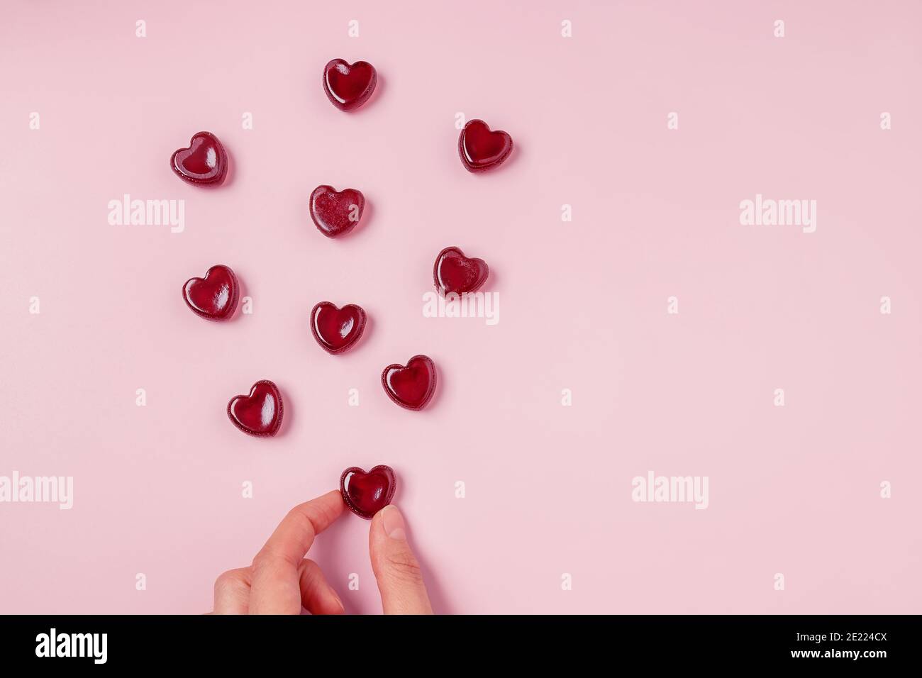 Main tenant l'une des bonbons rouges en gelée éparpillées de coeur forme sur fond rose Banque D'Images
