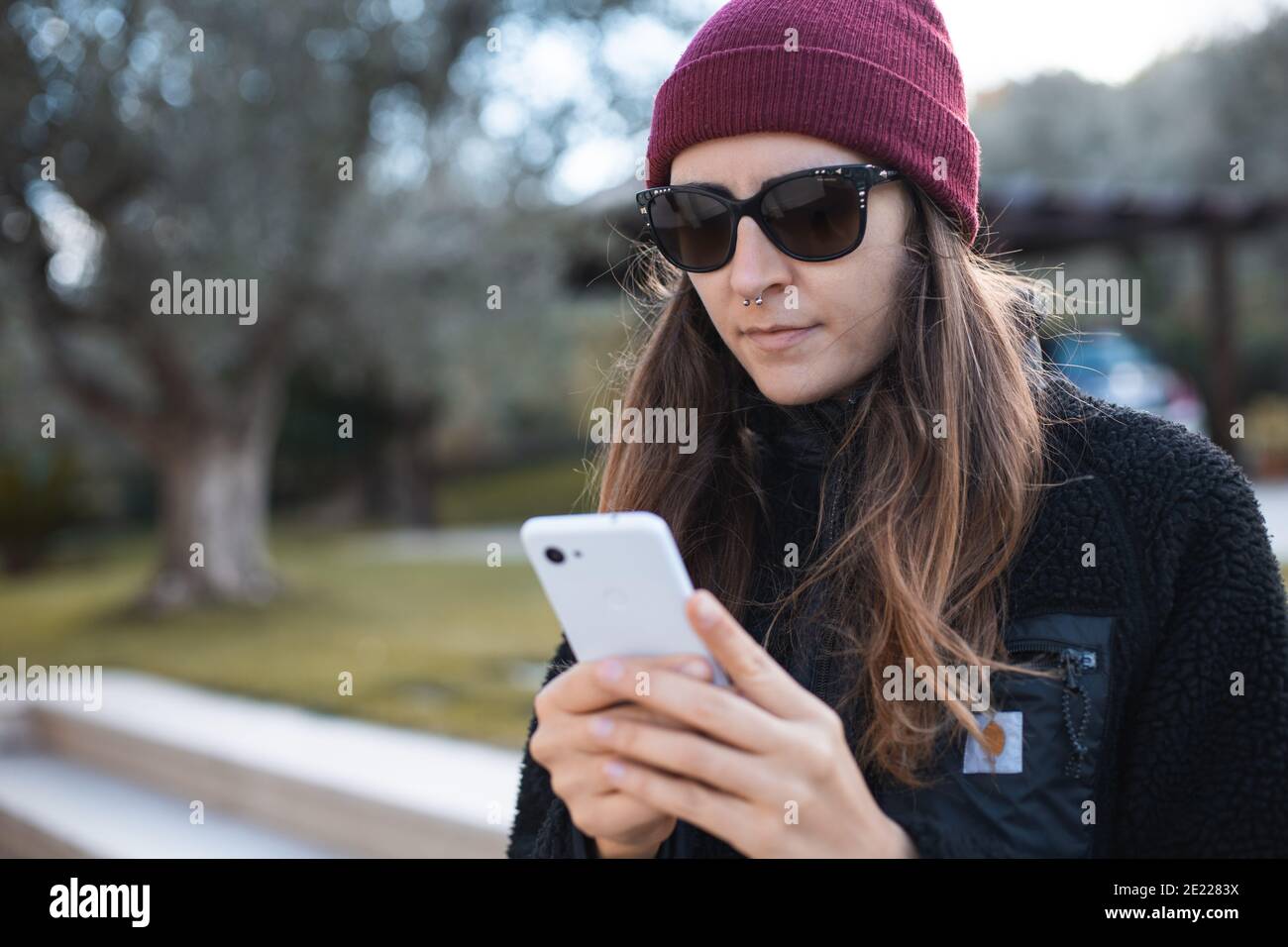 Femme portant un bonnet rouge et des lunettes de soleil à l'aide d'un  téléphone portable extérieur Photo Stock - Alamy