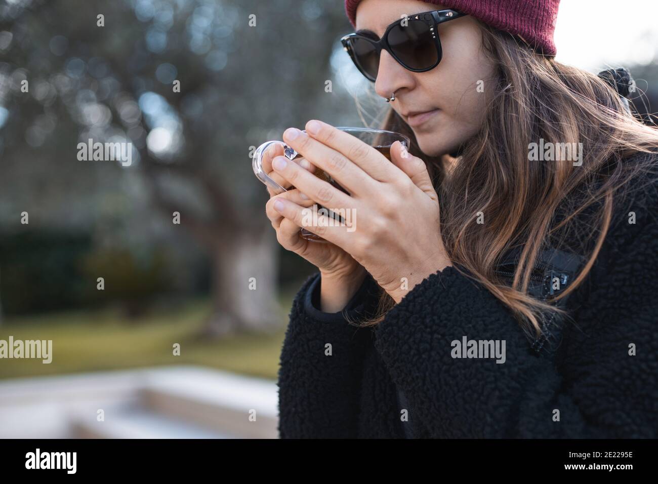 Femme portant un bonnet rouge et des lunettes de soleil buvant du thé à  l'extérieur Photo Stock - Alamy