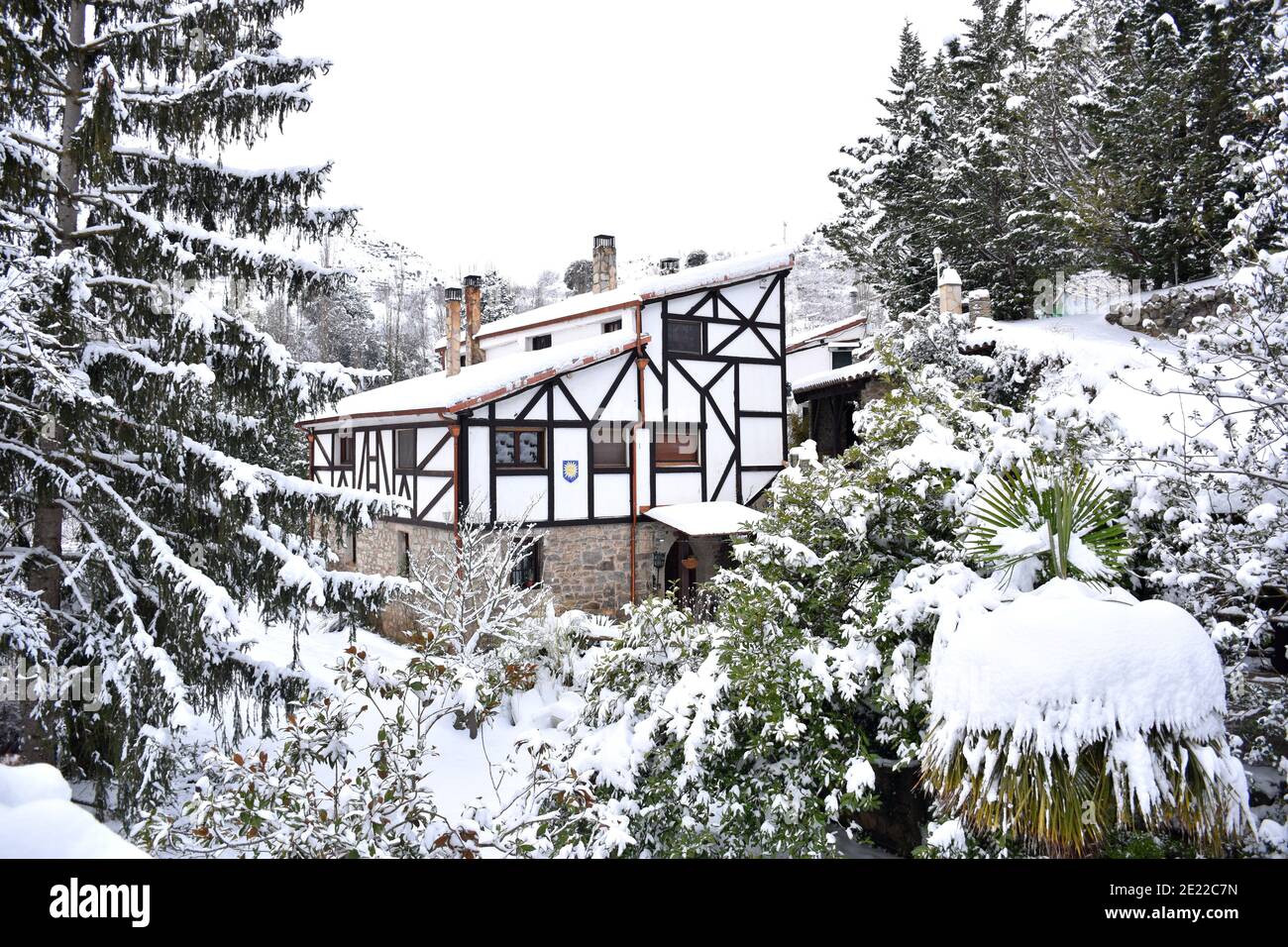 Photo de carte postale avec maison blanche avec dormeuses en bois sur la façade, cadran solaire, arbres autour. Tous couverts de neige après le passage des neiges Banque D'Images