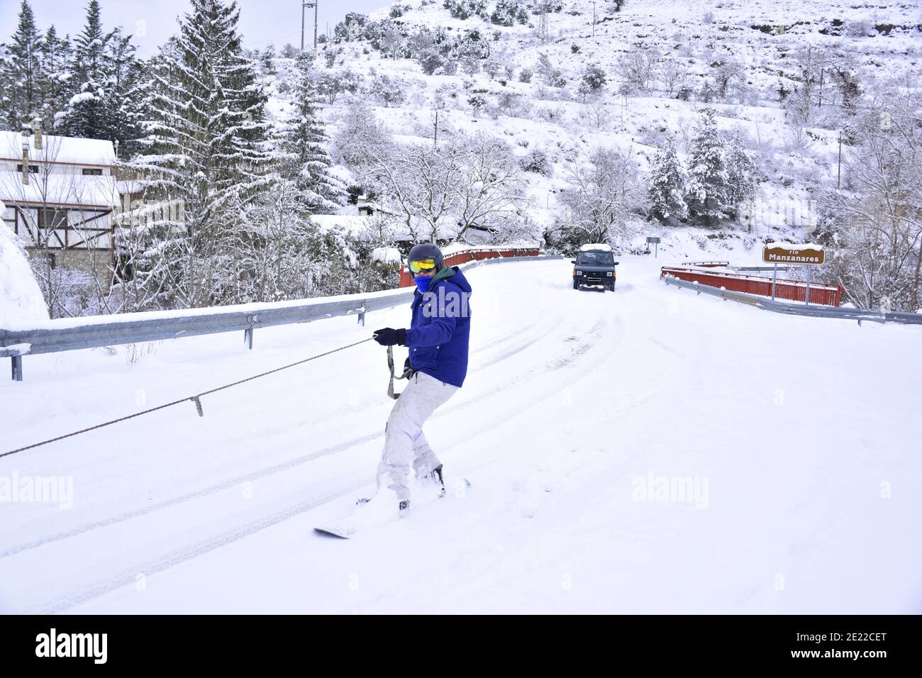 Homme dans une veste bleue de snowboard fixé par une corde à un véhicule. Neige sur une route principale à la Rioja. Tempête de neige de Filomena, Espagne, janvier 2021. Banque D'Images