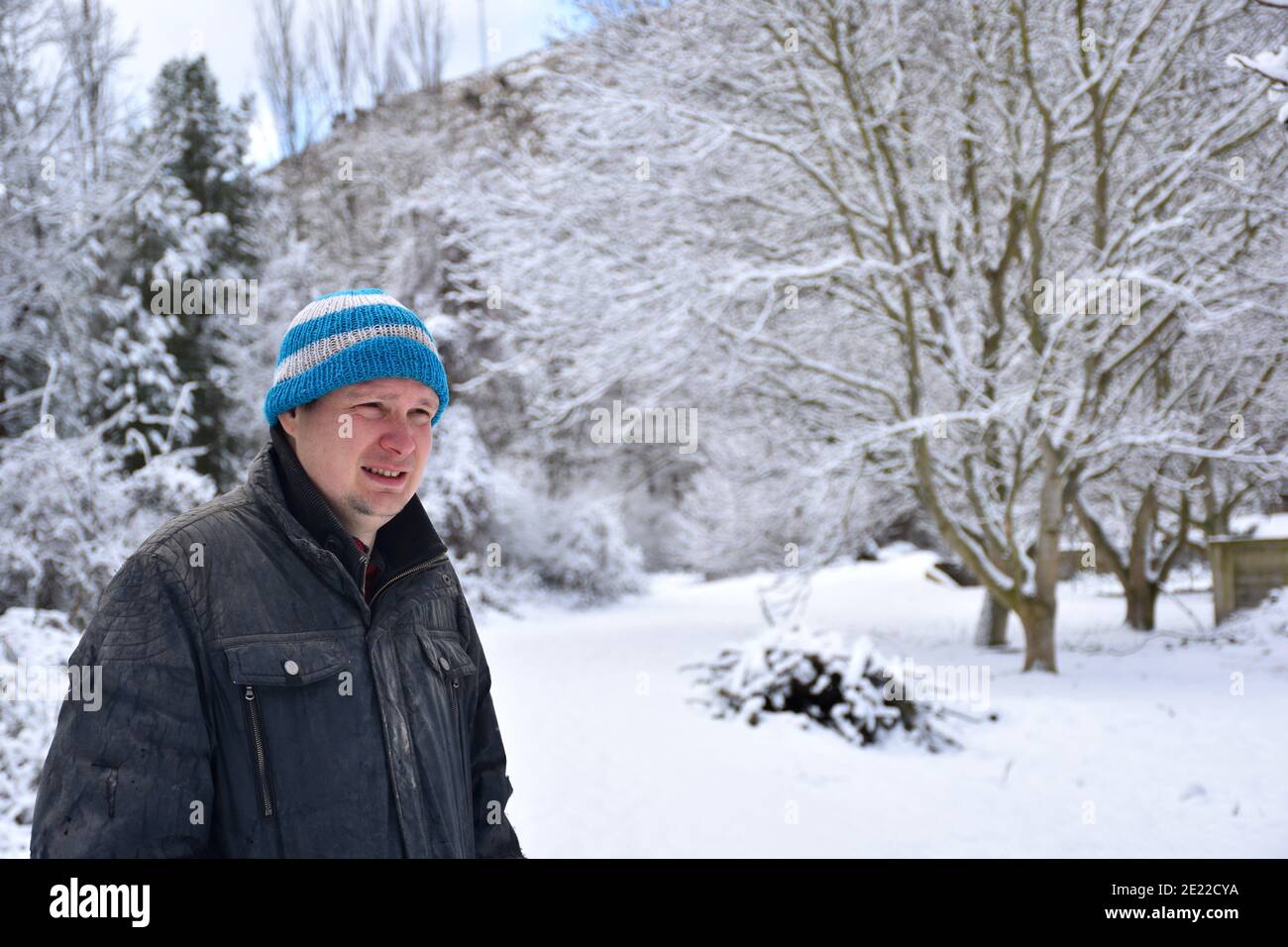 Portrait d'un homme au visage froid, vêtu d'une veste ancienne et déchirée et d'une casquette en laine bleue et blanche dans une région enneigée. Filomena temporaire. Banque D'Images