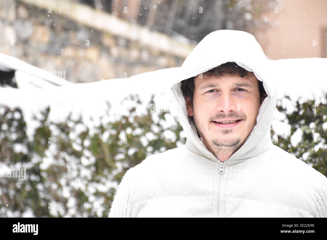 Portrait d'un homme souriant à côté de buissons enneigés. Vêtu d'une veste blanche, cheveux bruns et cheveux gris. Filomena temporaire. Banque D'Images