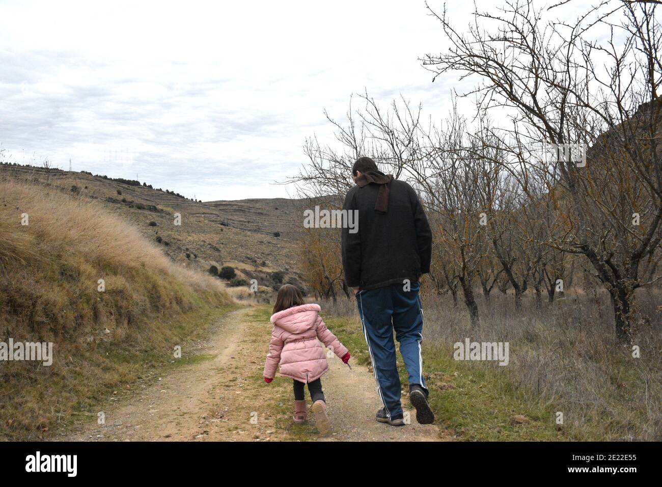 Jeune fille de cinq ans qui court avec son père sur une route de campagne. Vêtu de vêtements chauds en hiver. Banque D'Images