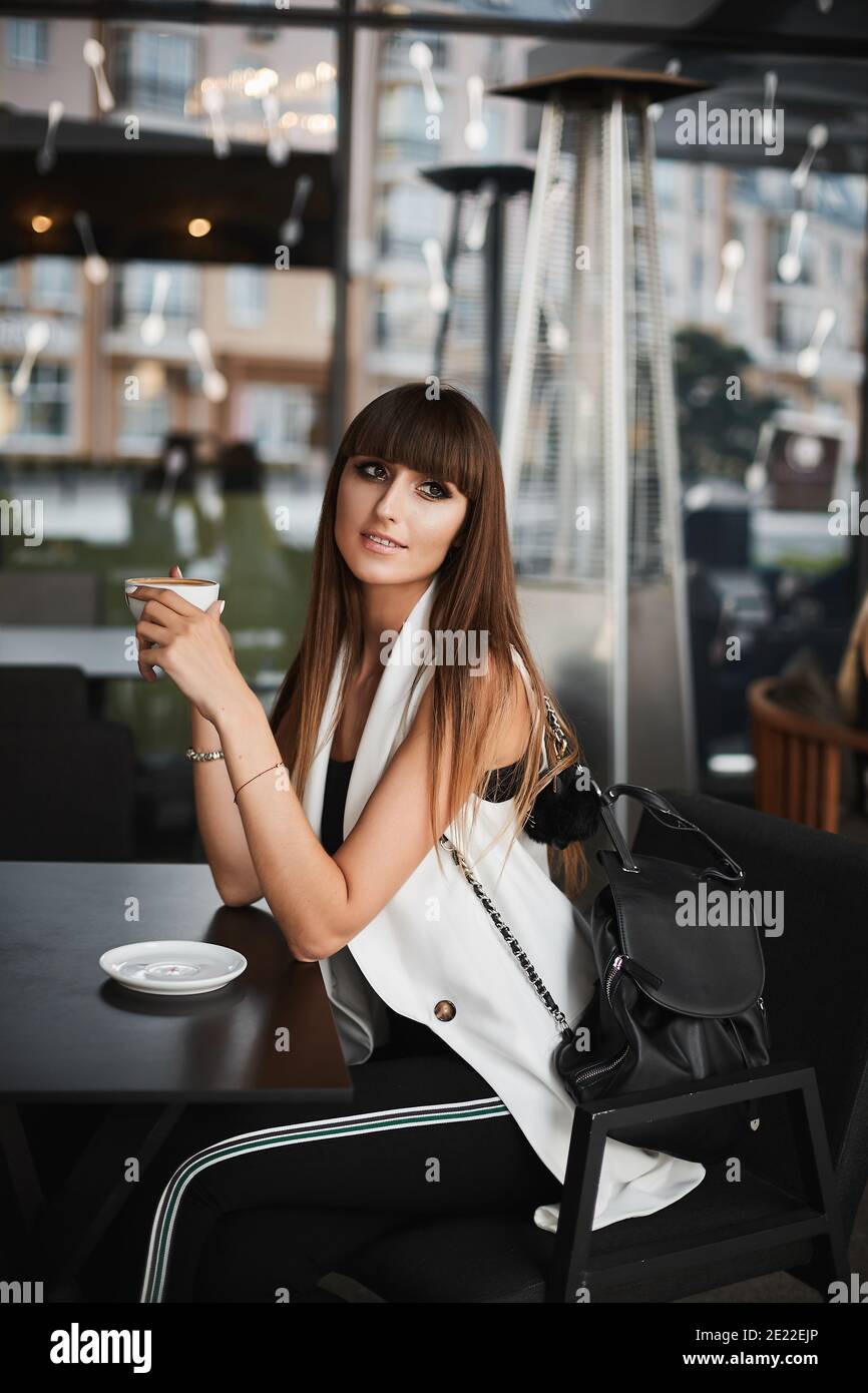 Jeune femme de race mixte avec un maquillage brillant dans un blanc la  veste sans manches est idéale pour faire une pause et boire un café chaud  un café vide à l'extérieur