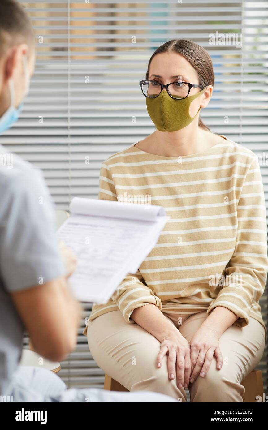 Portrait vertical de la jeune femme portant un masque et écoutant médecin en file d'attente à la clinique médicale Banque D'Images