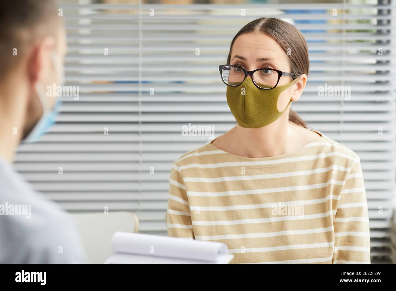Portrait vertical de la jeune femme portant un masque et écoutant médecin en file d'attente à la clinique médicale Banque D'Images