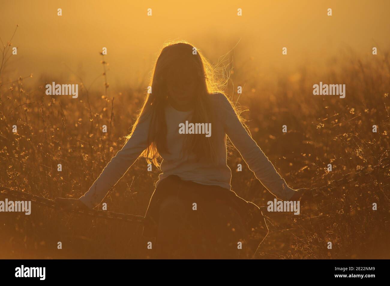 La jeune fille Blonde est assise sur une chaîne dans un or coucher de soleil Banque D'Images