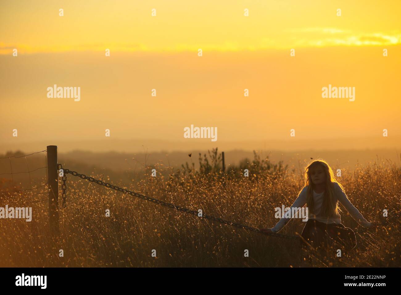 La jeune fille Blonde est assise sur une chaîne dans un or coucher de soleil Banque D'Images
