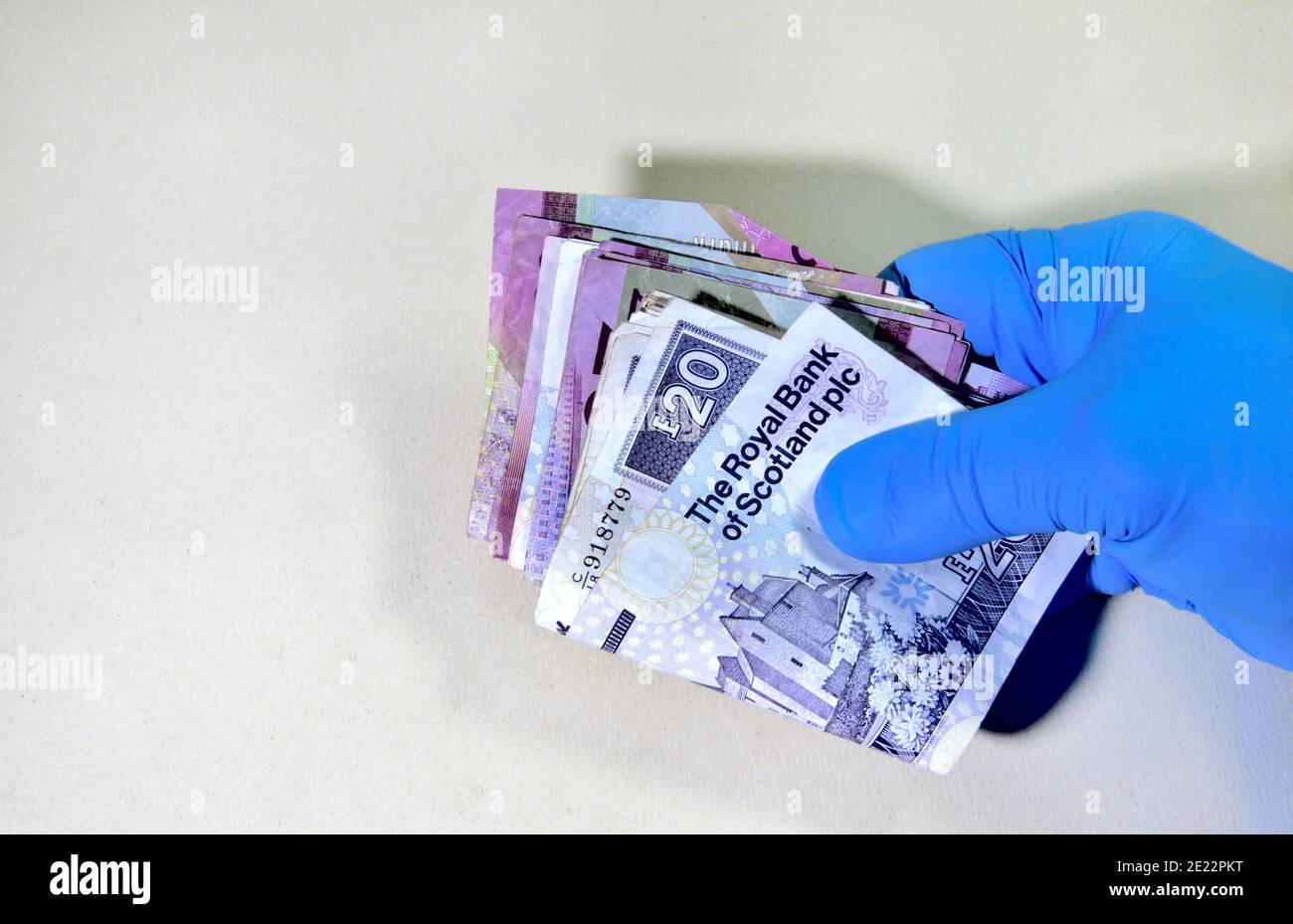 Main dans un gant de protection en caoutchouc tenant pile de billets de banque britannique, écossais, papier Banque D'Images