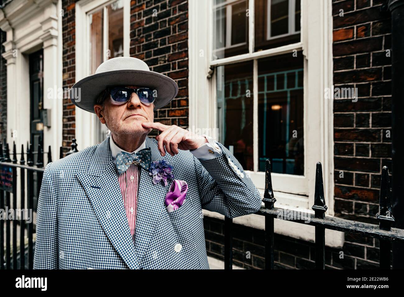 L'artiste George Skeggs (« soho George ») repose contre une rampe de fer sur Dean St, Soho, Londres, Angleterre, Royaume-Uni Banque D'Images