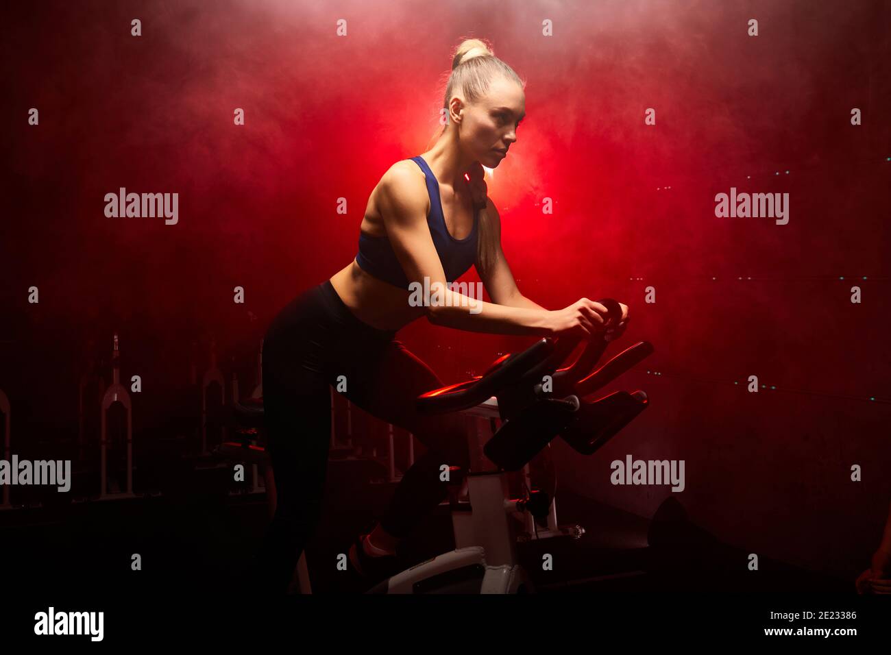 faites de la femme à la salle de gym, en faisant de l'exercice seul, dans une pièce enfumée avec des néons rouges Banque D'Images