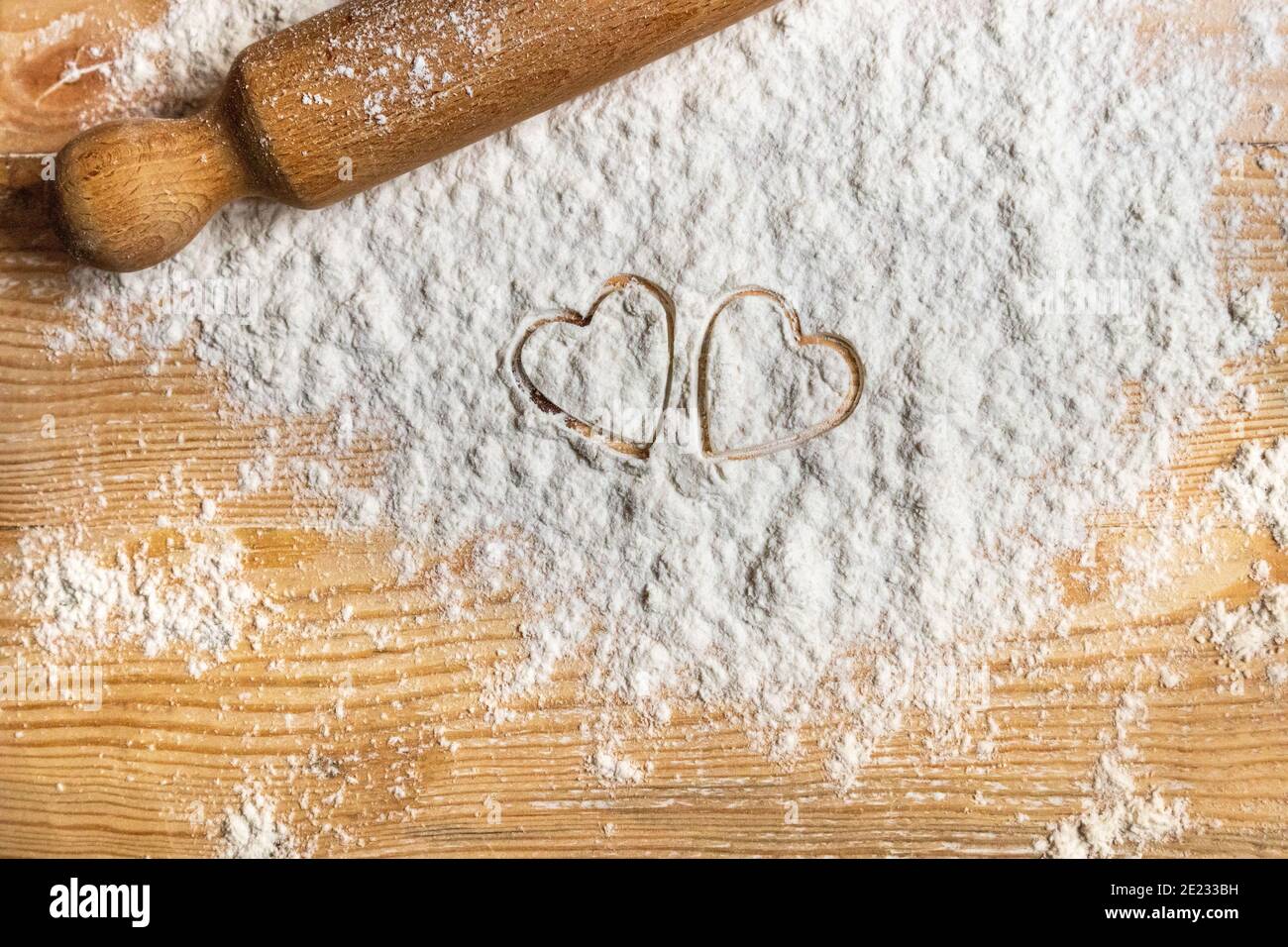 Préparez des biscuits pour le plus doux jour de l'année : la Saint-Valentin. Deux coeurs imprimés sur la farine dispersée sur une table en bois. Répandez l'amour ! Banque D'Images