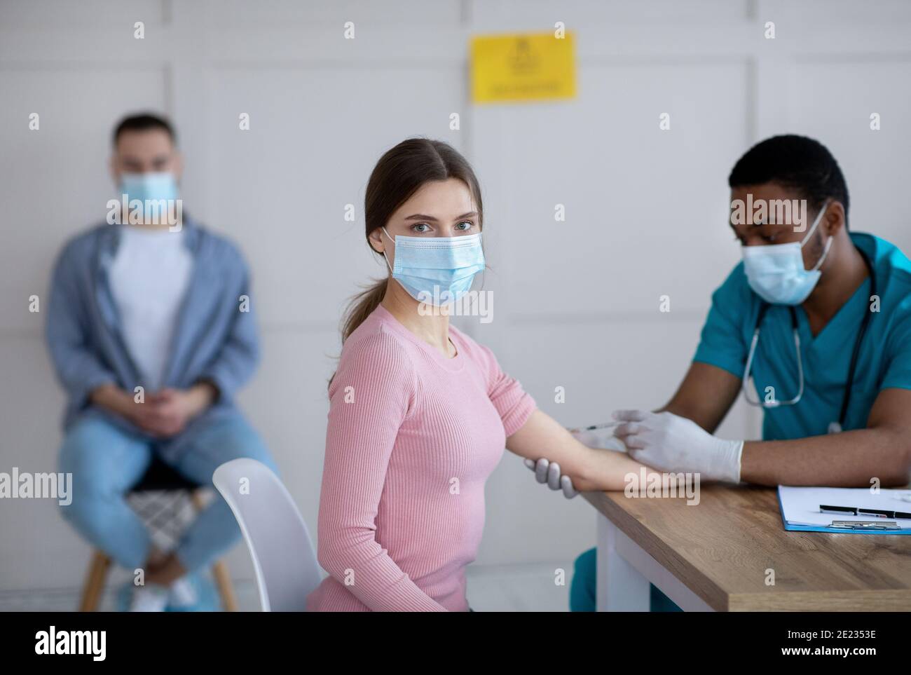 Un médecin de sexe masculin noir donne une injection intramusculaire à une jeune femme à bureau médical Banque D'Images