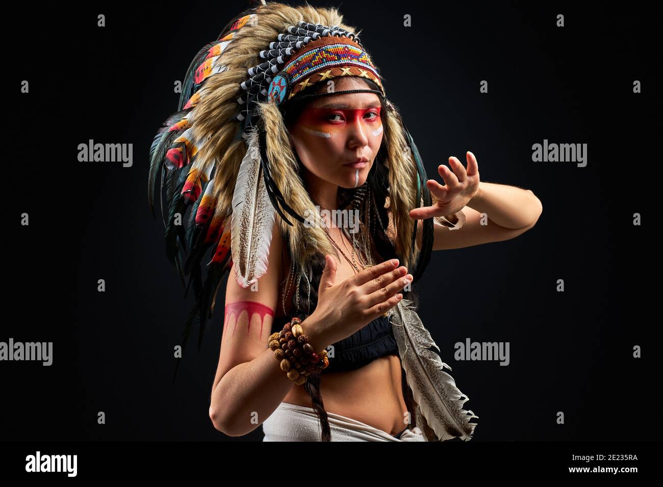 Modèle en port indien et maquillage coloré posant à la caméra, avec des plumes sur la tête. Tenue des peuples autochtones des Amériques, femme ethnique Banque D'Images