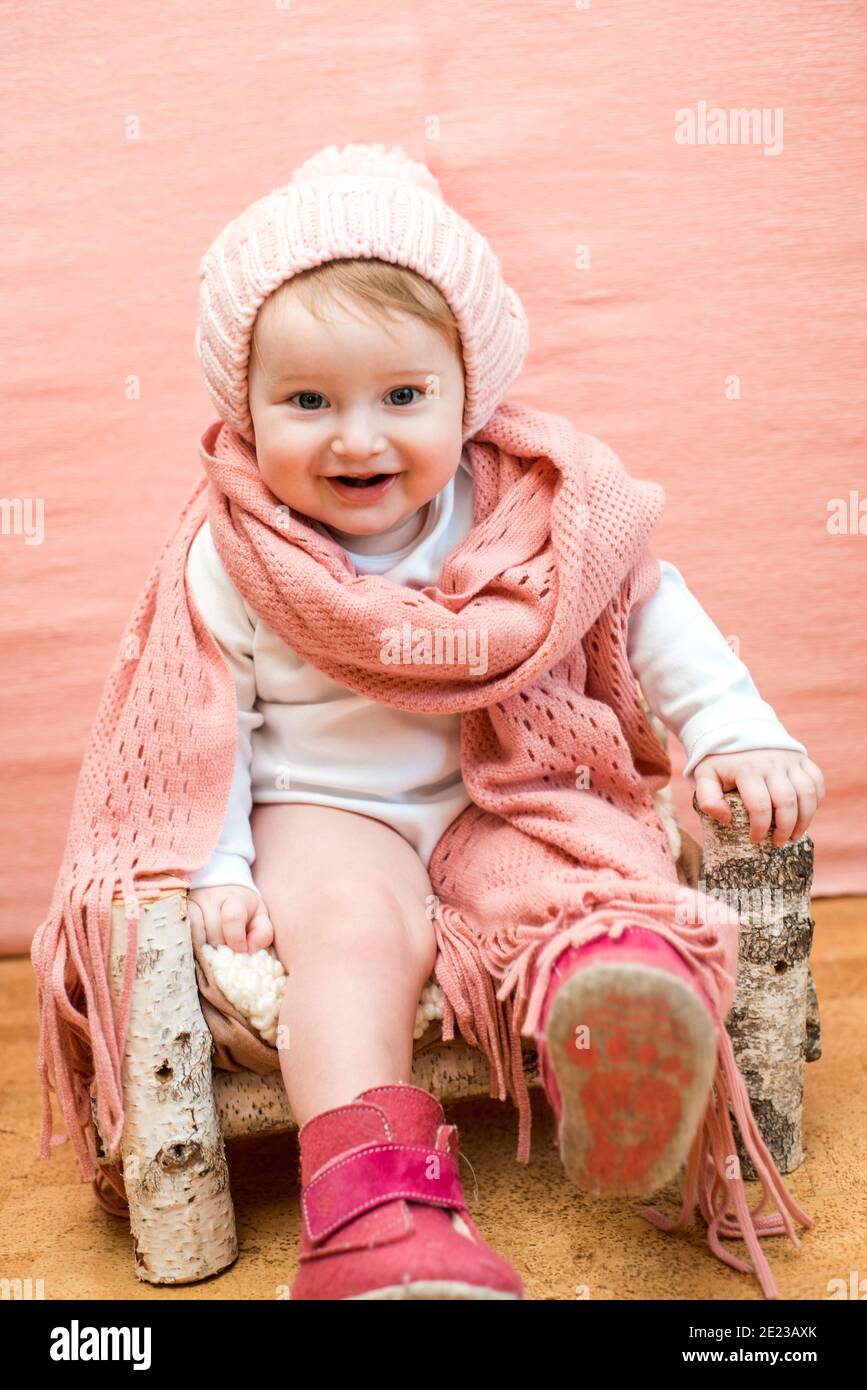 Gros plan sur le visage de bébé dans la écharpe tube. Petite fille mignonne  avec des yeux bleus dans un bonnet tricoté rose et une écharpe sur fond  rose.confortable hiver chaud ou